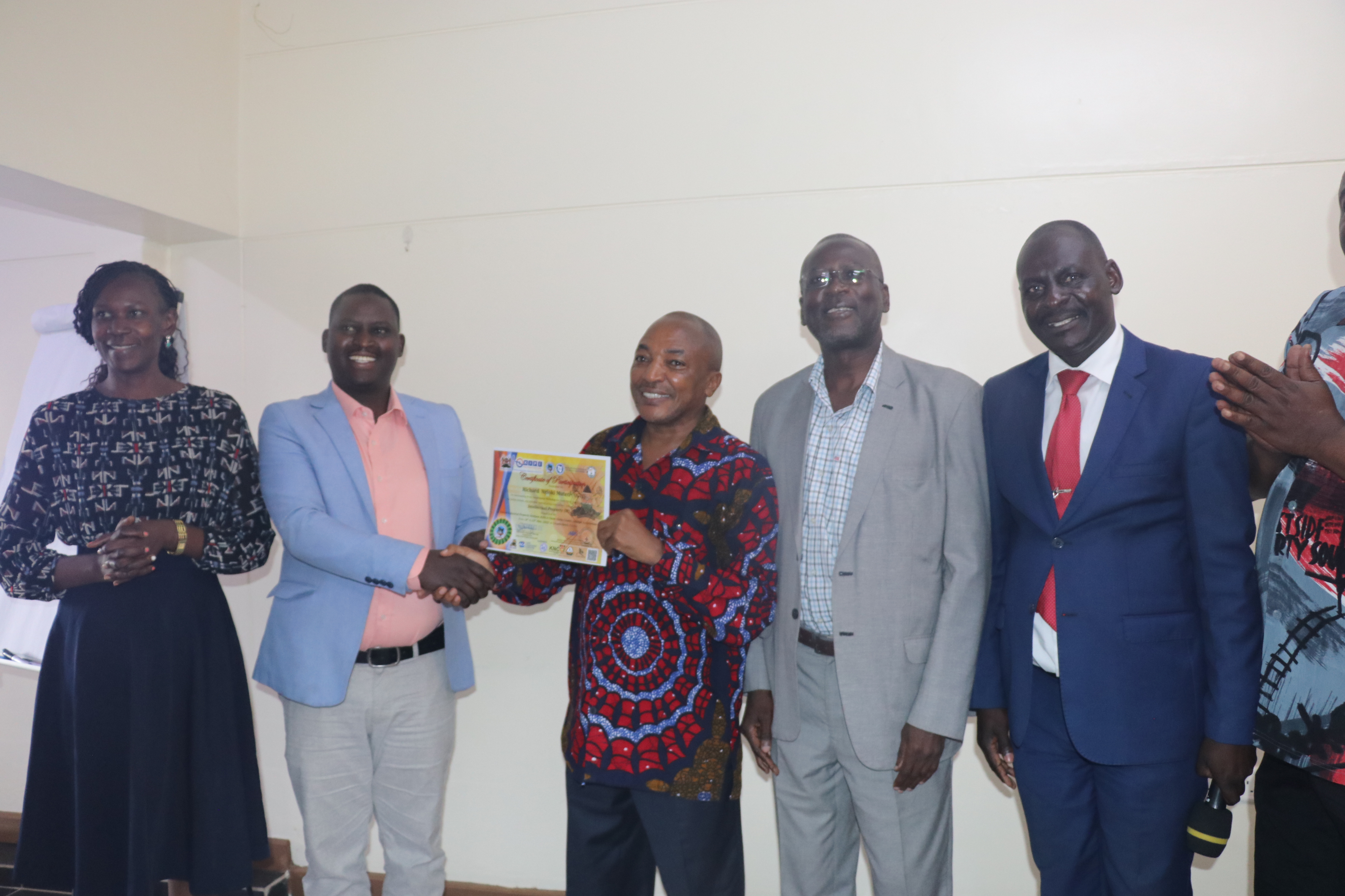 Alton Kogo (2nd Left), Director North Rift, Micro and Small Enterprises Authority (MSEA), hands over a certificate of participation to Richard Muteti, Chairman of the Skilled Artisans and Informal Apprenticeship Association-Kenya Chapter. They are flanked by Antoninah Makoba (Left), Chairlady of Fashions and Design Association, John Onyango (3rd Right), KIPI MD and  Richard Opar (2nd Right), KNFJKA Secretary General, Uasin Gishu Chapter during the closing ceremony of the Workshop